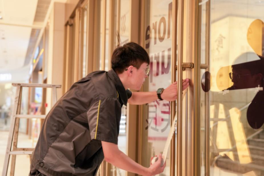 商场工作人员为部分大门贴密封条，减少冷气流出。